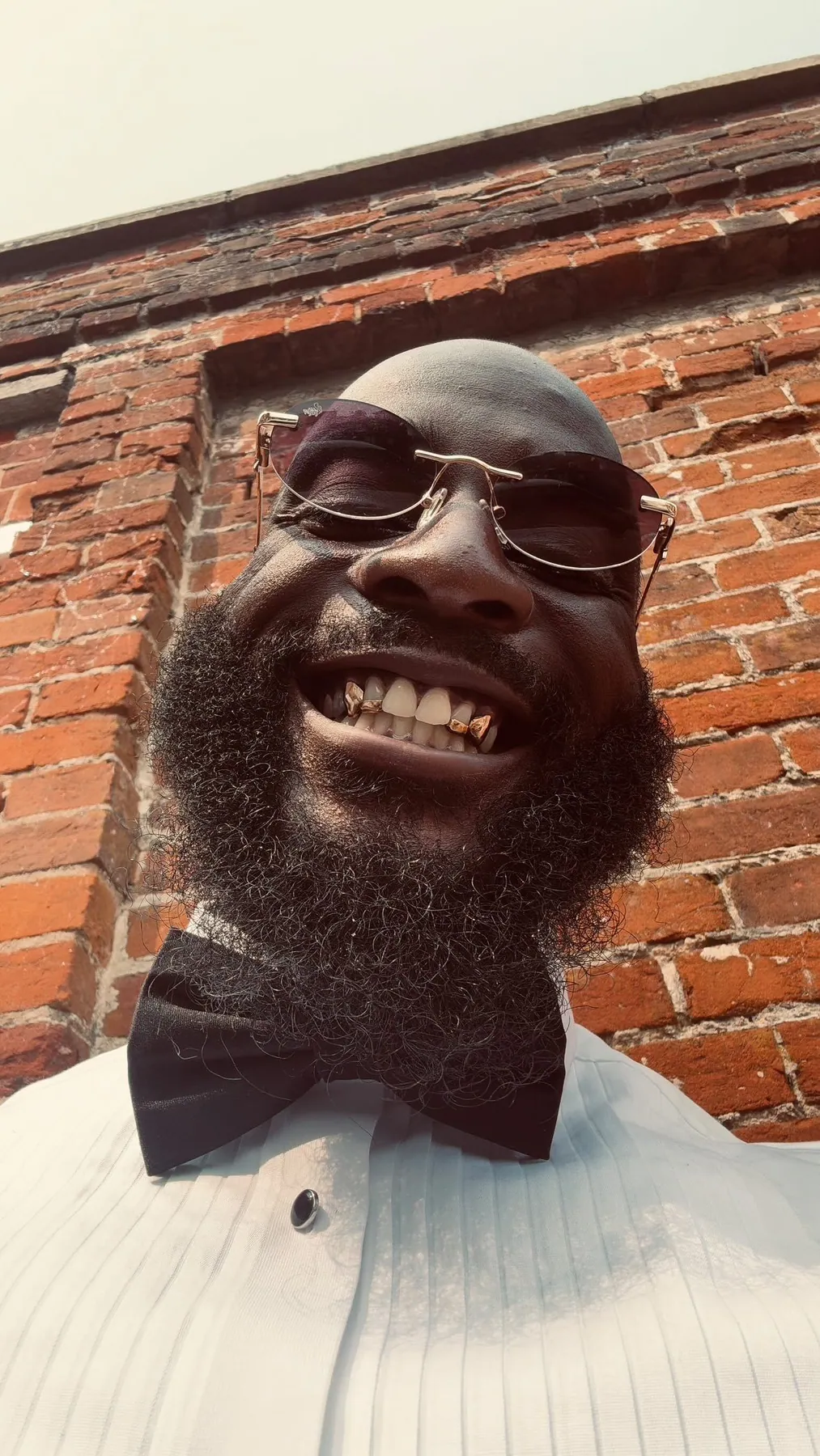 A Matrix client in a bow tie and tinted glasses, laughing and showing gold grillz on his front teeth