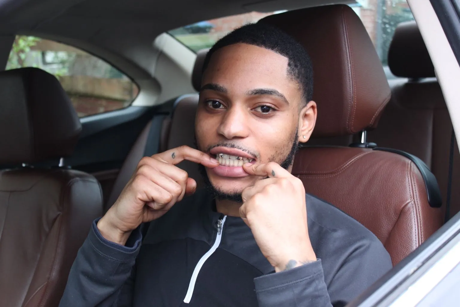 A Matrix client in a car pulling his lip to show his grillz