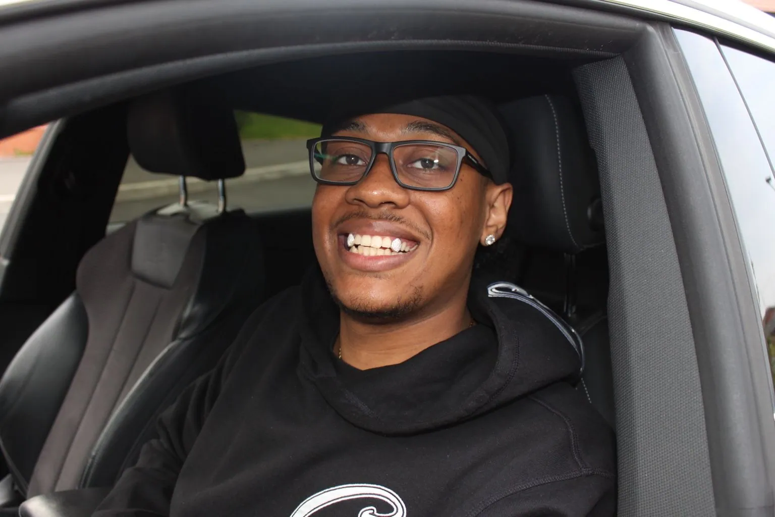 A Matrix client in glasses smiling from a car, with diamond-set canine grillz