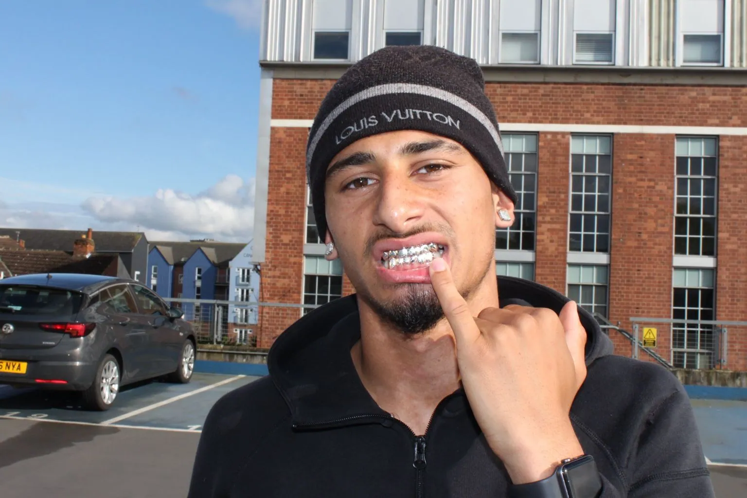 A Matrix client in a beanie showing a diamond-set grillz set in a car park