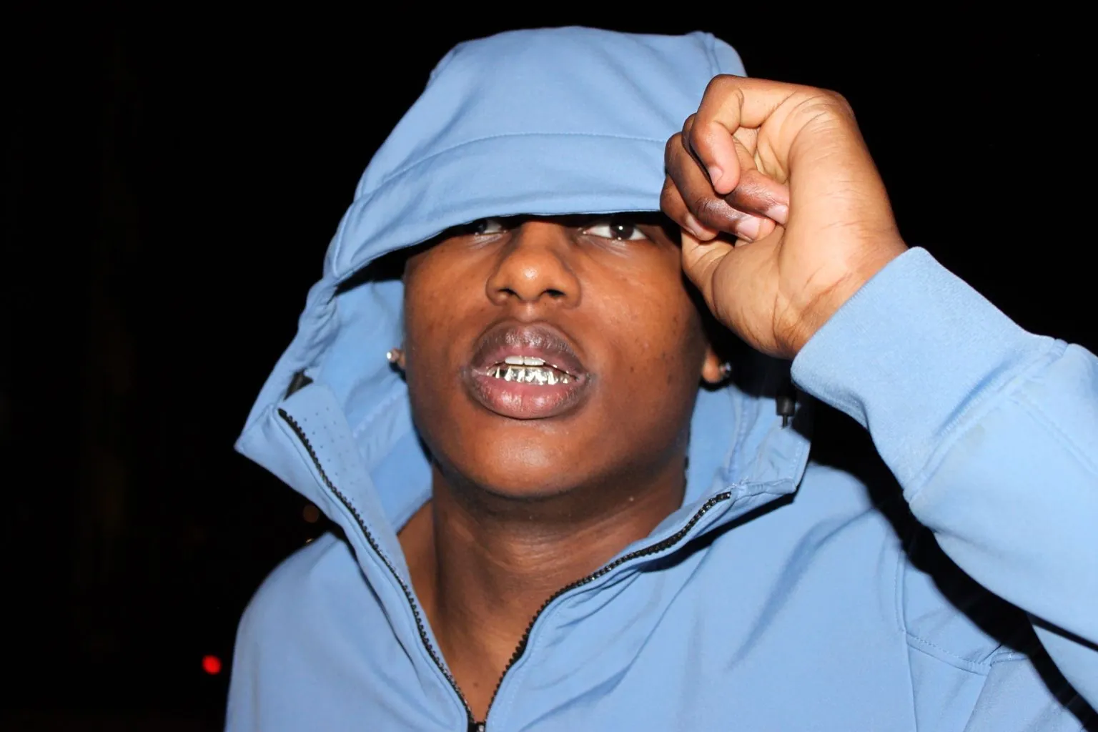 A Matrix client in a blue hoodie at night, showing his grillz