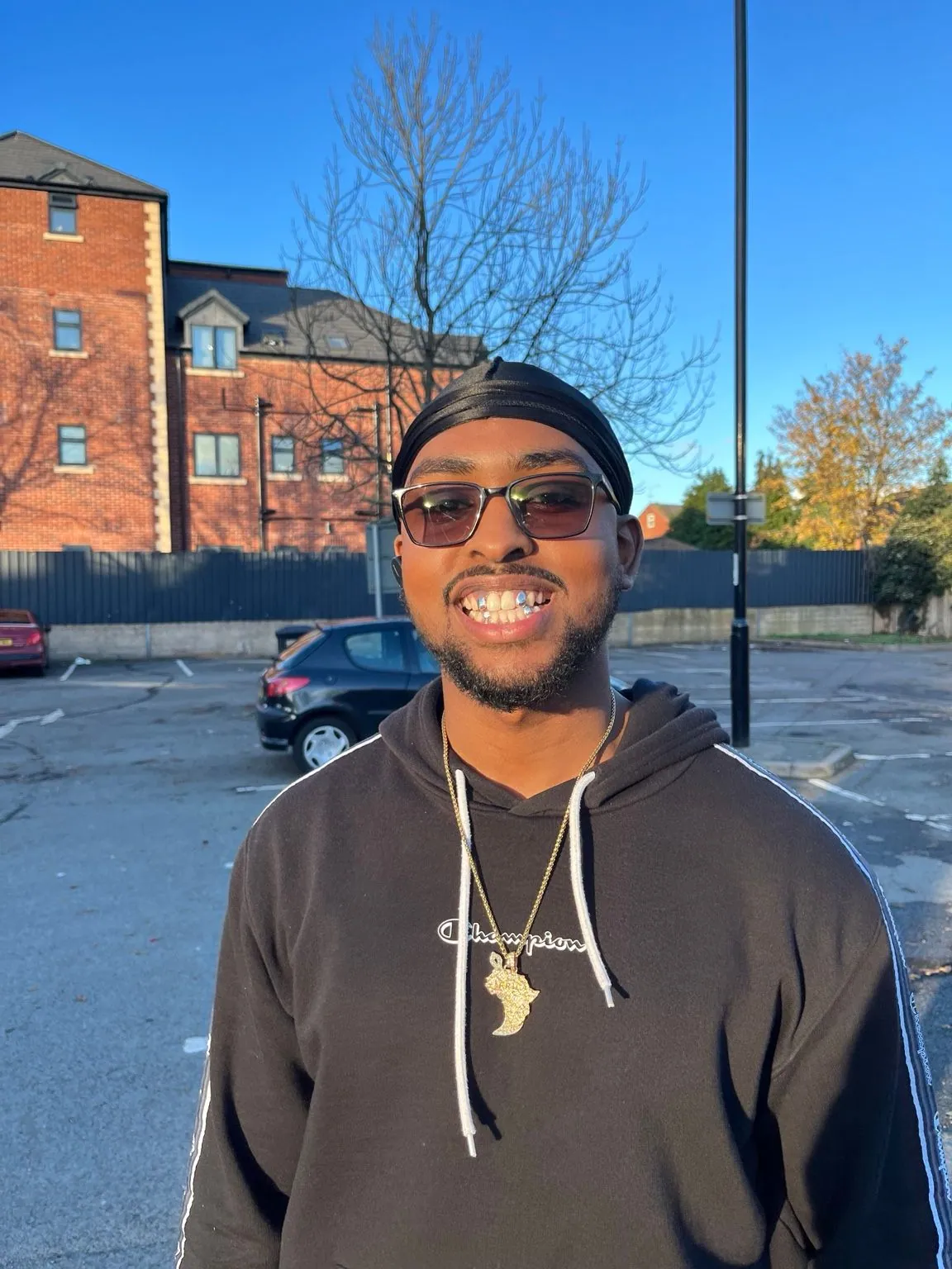 A Matrix client in sunglasses outdoors, smiling with a grillz set