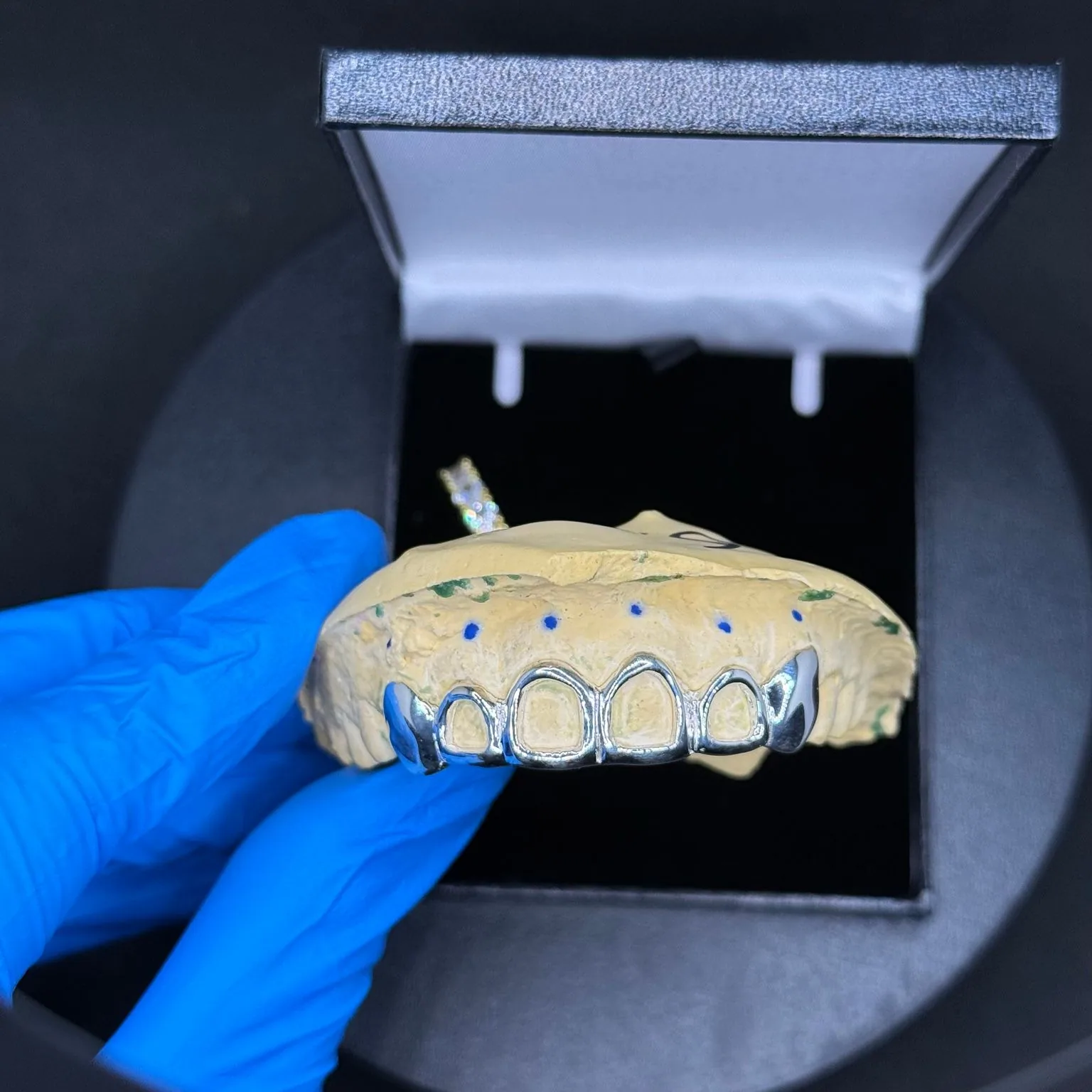A finished Window-style grillz set resting on a dental model in a jewellery box, held by a gloved hand