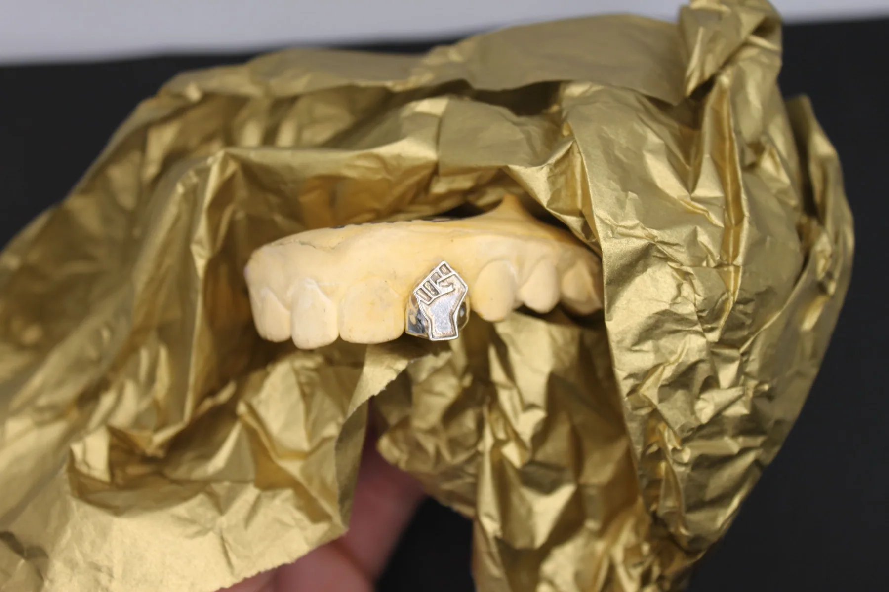A custom raised-fist tooth cap on a dental stone model, resting in gold tissue paper