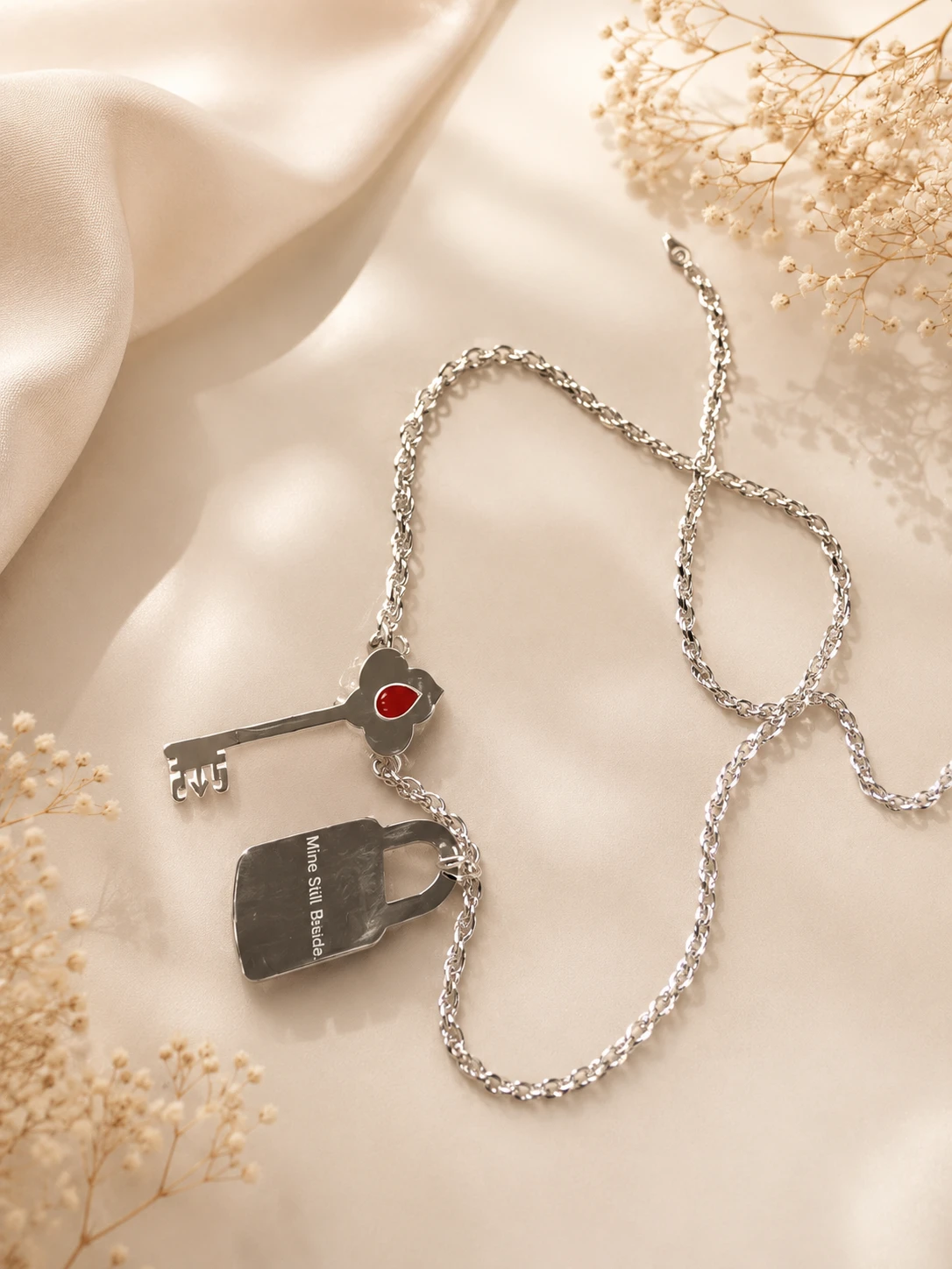 A silver rope chain with a key and padlock pendant with red enamel, on warm cream fabric