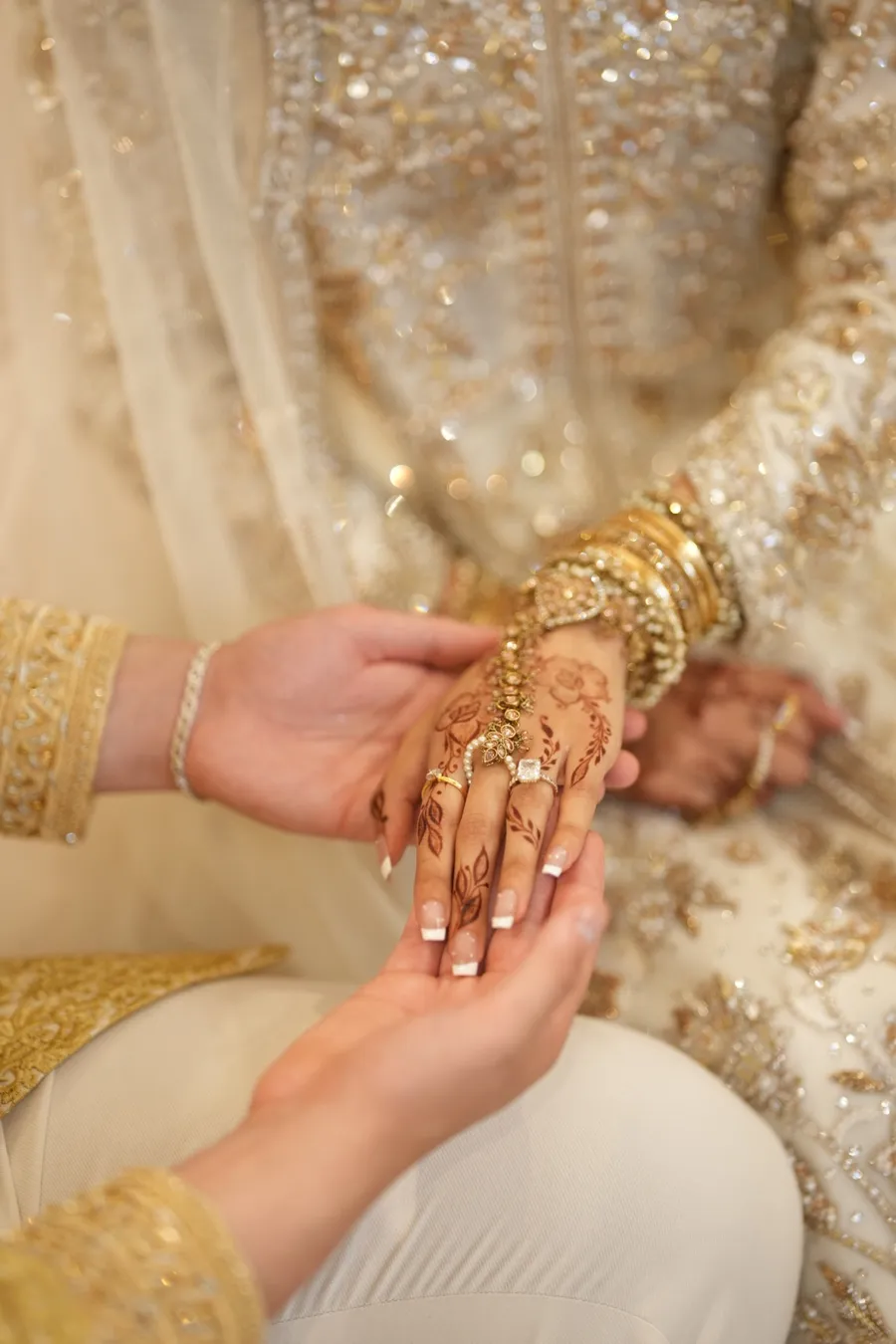 Close-up of one hand holding another hand decorated with henna and set with a stone ring and a gold ring, with gold bangles, at a wedding